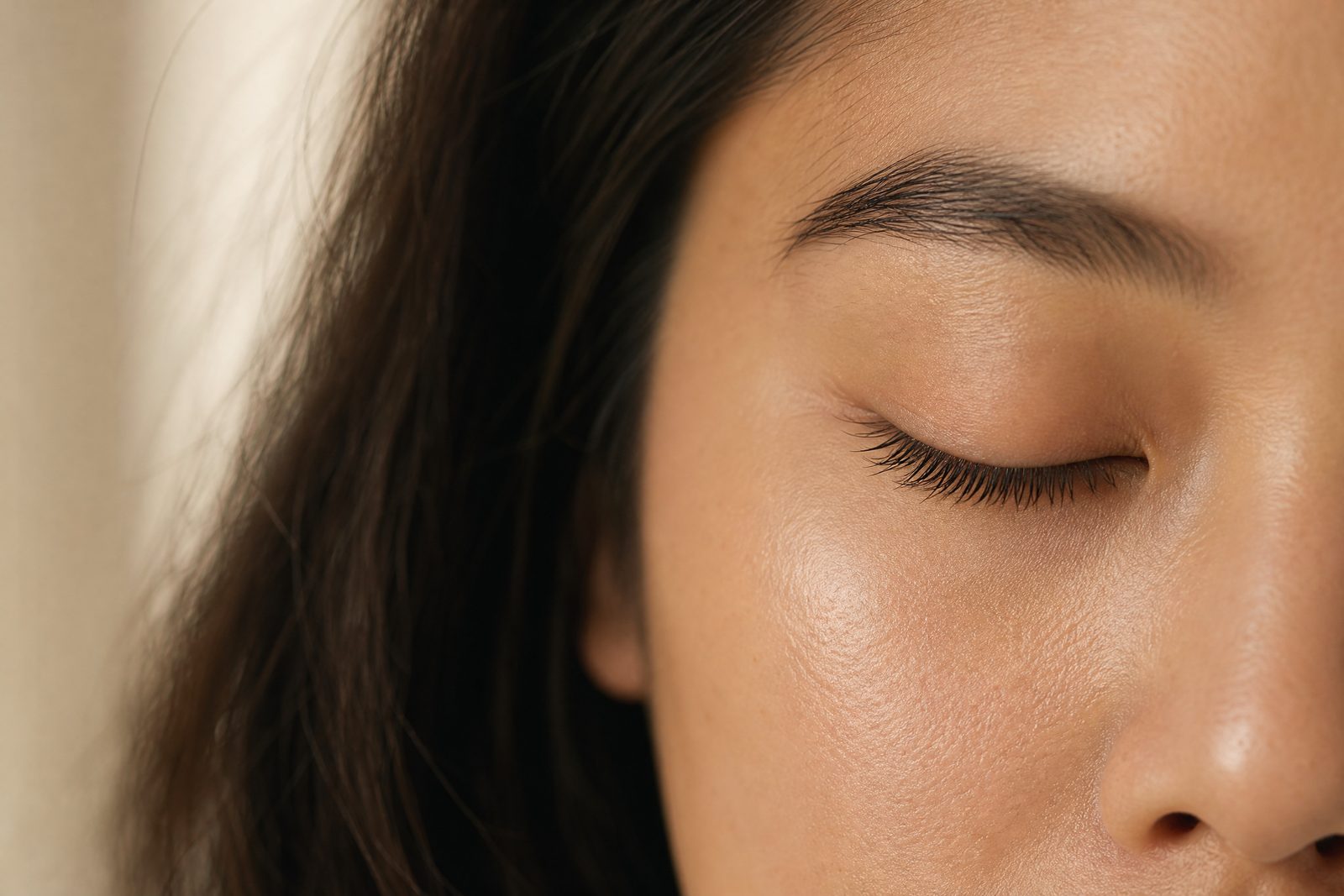 Close crop of a woman's closed eye in warm sunlight, her natural lashes lifted into a soft curl.